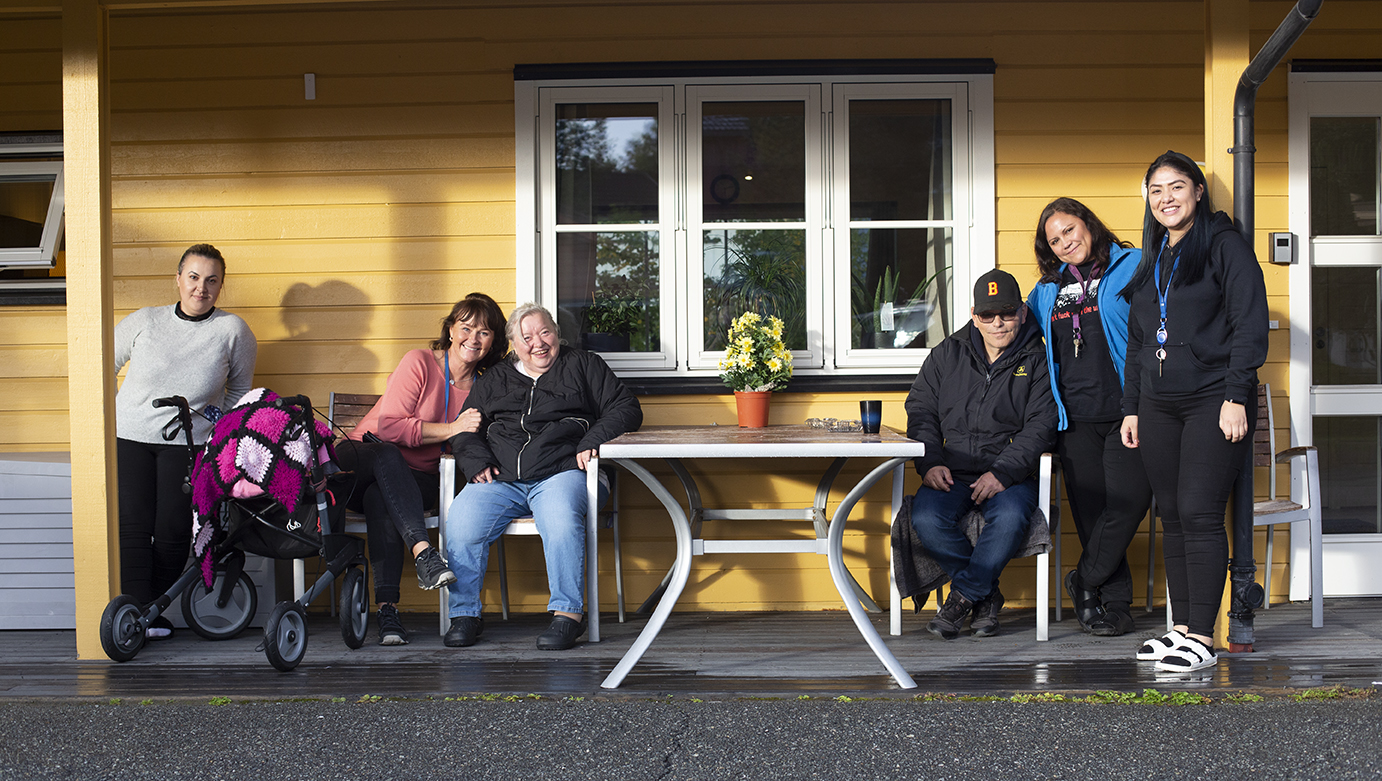 Bilde av mennesker utenfor et hus som ser i kamera og smiler