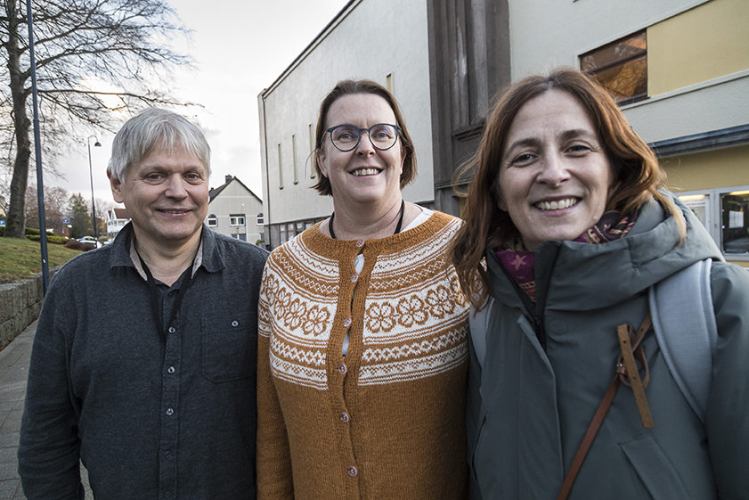 En mann og to damer står ute foran et hus. Alle tre smiler. 