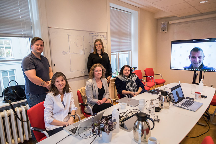 Bilde av fire personer i et møterom, og en perosn deltar gjennom skjerm. Alle smiler og ser mot kameraet. ©Otto von Munchow