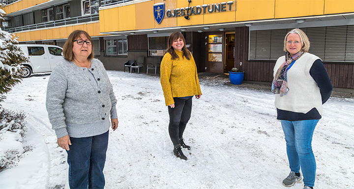 Tre damer står utenfor en bygning. De står i en bue med litt avstand mellom hverandre. Alle ser i kameraet og smiler. 