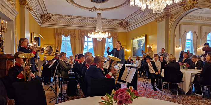 Vi ser et korps fra siden. De spiller inne, og mennesker sitter i bakgrunnen og ser mot de. 